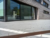 a very narrow path in front of a brick building with large glass doors and a bench in the middle