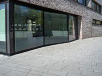 a very narrow path in front of a brick building with large glass doors and a bench in the middle