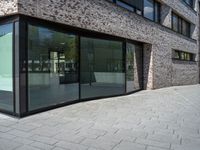 a very narrow path in front of a brick building with large glass doors and a bench in the middle