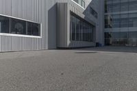 the side of a warehouse building next to a bicycle racket and garbage can on a concrete ground