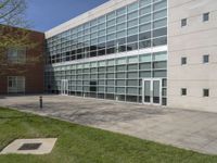 a building with large windows near the grass outside the building is made from concrete and has some glass on it