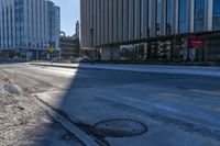 an empty street in front of tall buildings and a pot hole on the street corner