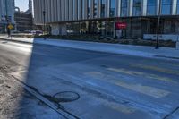 an empty street in front of tall buildings and a pot hole on the street corner