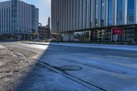 an empty street in front of tall buildings and a pot hole on the street corner