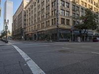 cars drive down the street in front of the tall building with glass windows on the third story