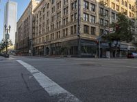 cars drive down the street in front of the tall building with glass windows on the third story