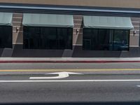 a street with white lines that look like a road sign pointing to an intersection where two buildings, one with large windows, are reflected in the sun