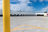 a large storage building under a cloudy blue sky with yellow painted lines around the entrance