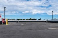 an empty parking lot with many lights and some trees in the distance, near a large building