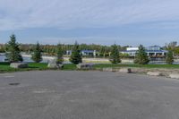 a paved parking lot in a park with benches and tree lined trees surrounding it with blue sky in the background