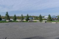 a paved parking lot in a park with benches and tree lined trees surrounding it with blue sky in the background