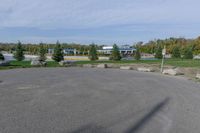 a paved parking lot in a park with benches and tree lined trees surrounding it with blue sky in the background