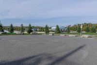 a paved parking lot in a park with benches and tree lined trees surrounding it with blue sky in the background