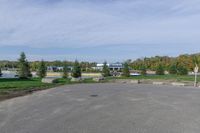 a paved parking lot in a park with benches and tree lined trees surrounding it with blue sky in the background