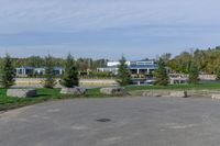 a paved parking lot in a park with benches and tree lined trees surrounding it with blue sky in the background