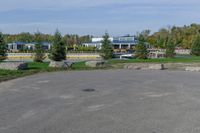 a paved parking lot in a park with benches and tree lined trees surrounding it with blue sky in the background