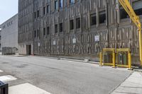 an industrial building with some yellow barriers in the middle of it on the street in front of it is a trash can and sign