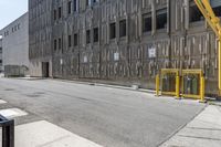 an industrial building with some yellow barriers in the middle of it on the street in front of it is a trash can and sign