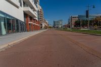 an empty street is pictured on the sidewalk outside of a building in the background, a parking meter and lots of glass