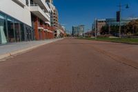 an empty street is pictured on the sidewalk outside of a building in the background, a parking meter and lots of glass