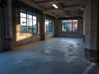 a room with two large windows and cement floors in it next to some trash cans