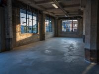 a room with two large windows and cement floors in it next to some trash cans