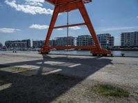 an orange crane is sitting in the field by some water and buildings on a sunny day