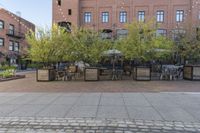 an empty cobblestone walkway at an outdoor restaurant and patio area in front of brick buildings