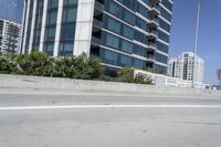a man riding his motorcycle on the road in front of a tall building with glass walls