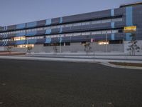 an empty road in front of a large modern building at twilight, with a blue stripe on the side