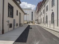 an empty sidewalk in between two very wide buildings and a few people walking around the corner