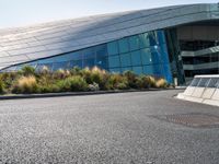 a large white building with a glass facade near the road of grass and bushes with metal trim