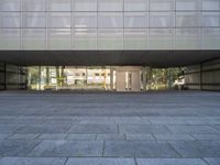 a stone walkway next to a concrete block floor under large glass windows and doors with a sculpture of a person in the background