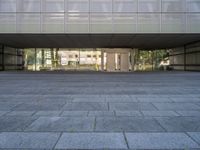 a stone walkway next to a concrete block floor under large glass windows and doors with a sculpture of a person in the background