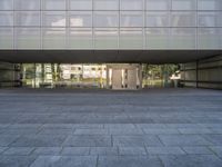 a stone walkway next to a concrete block floor under large glass windows and doors with a sculpture of a person in the background