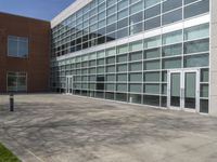 a building with large windows near a grassy area, surrounded by plants and bushes, is pictured in an empty area