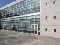 a building with large windows near a grassy area, surrounded by plants and bushes, is pictured in an empty area