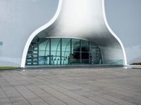 a very large modern building that is white and grey in color, with a clock attached to the side of it