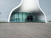 a very large modern building that is white and grey in color, with a clock attached to the side of it