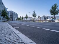 a long empty street is next to a large building that has an outdoor structure in the background