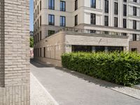 a brick building next to a parking area and bushes in front of it, and some people