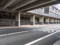 a deserted street under a bridge, near buildings in the city area, with a bus passing underneath the walkway