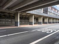 a deserted street under a bridge, near buildings in the city area, with a bus passing underneath the walkway