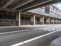 a deserted street under a bridge, near buildings in the city area, with a bus passing underneath the walkway