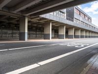 a deserted street under a bridge, near buildings in the city area, with a bus passing underneath the walkway