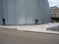 an empty road leading to a large building with a metal structure on one side and steps going up to the top