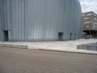 an empty road leading to a large building with a metal structure on one side and steps going up to the top