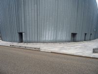 an empty road leading to a large building with a metal structure on one side and steps going up to the top