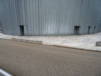 an empty road leading to a large building with a metal structure on one side and steps going up to the top
