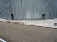 an empty road leading to a large building with a metal structure on one side and steps going up to the top